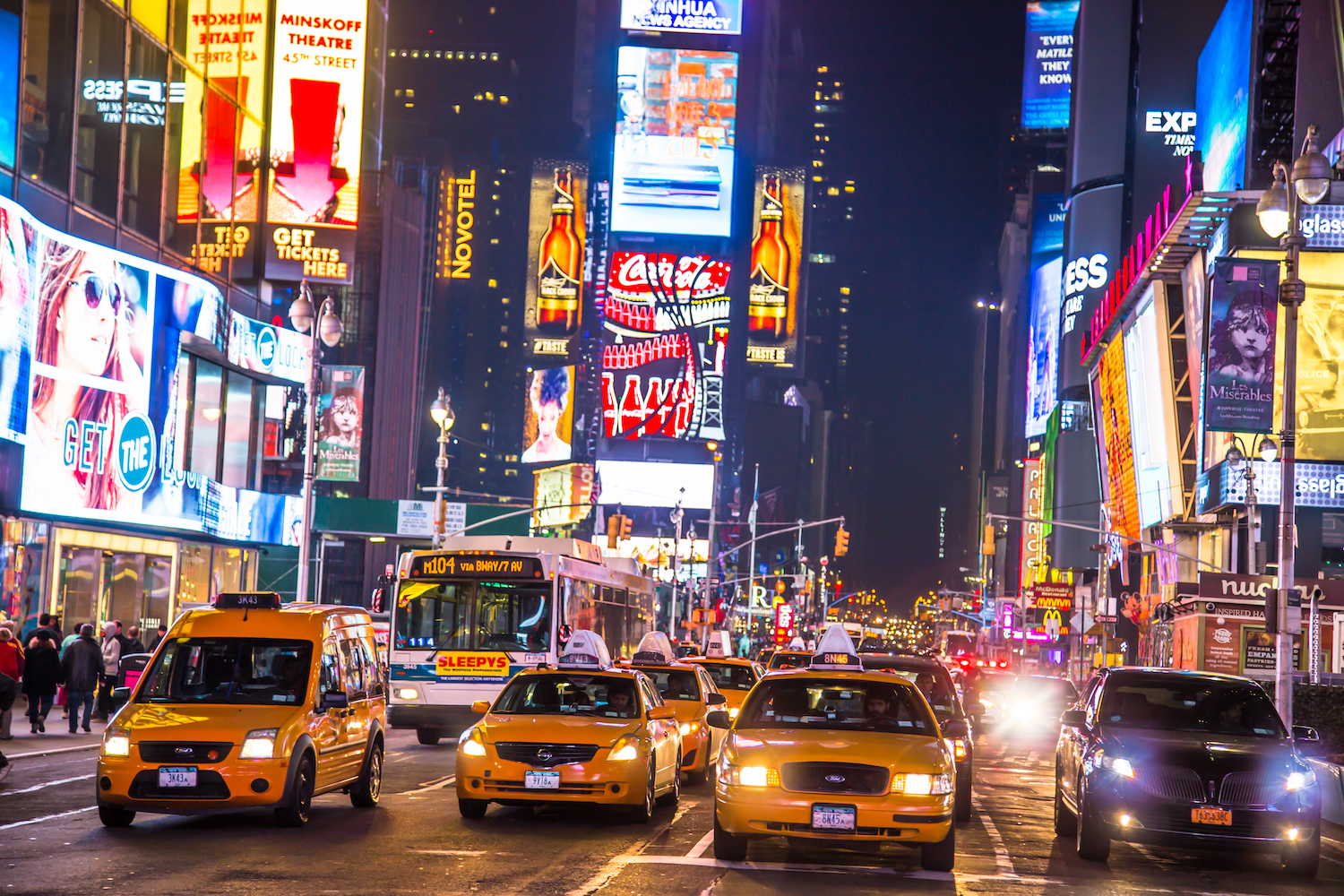 Traffic, taxis and buses parked bumper-to-bumper in times square at night, billboards visible in the background.