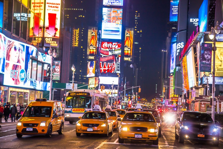 Traffic, taxis and buses parked bumper-to-bumper in times square at night, billboards visible in the background.