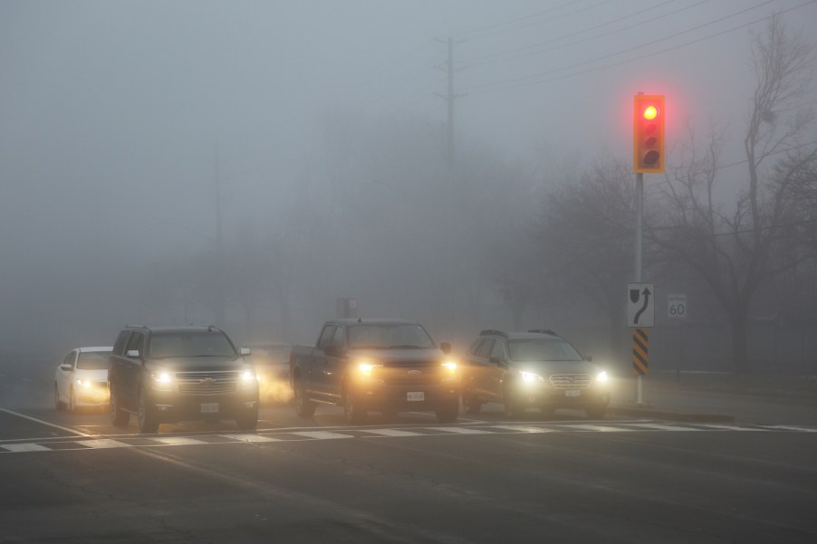 Cars driving in fog with their headlights on.