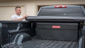 Man rolling up the tonneau cover on his pickup truck to reveal a Craftsman vault-style locking tool chest in the bed.