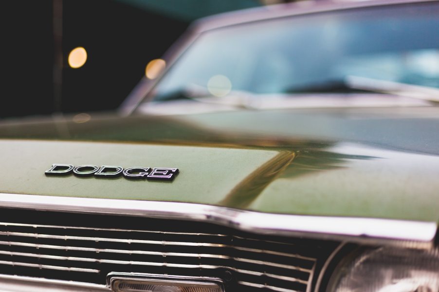 Closeup of the Dodge logo on a classic green muscle car, the chrome of its grille just visible in the foreground.