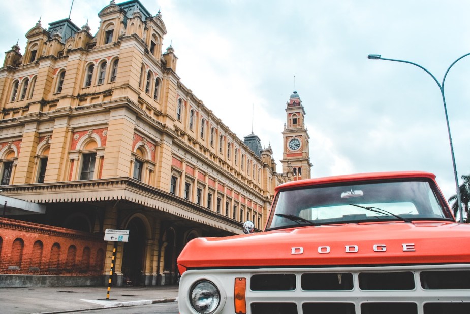 Classic red Dodge truck parked on the street, a sandstone-colored building visible in the background.