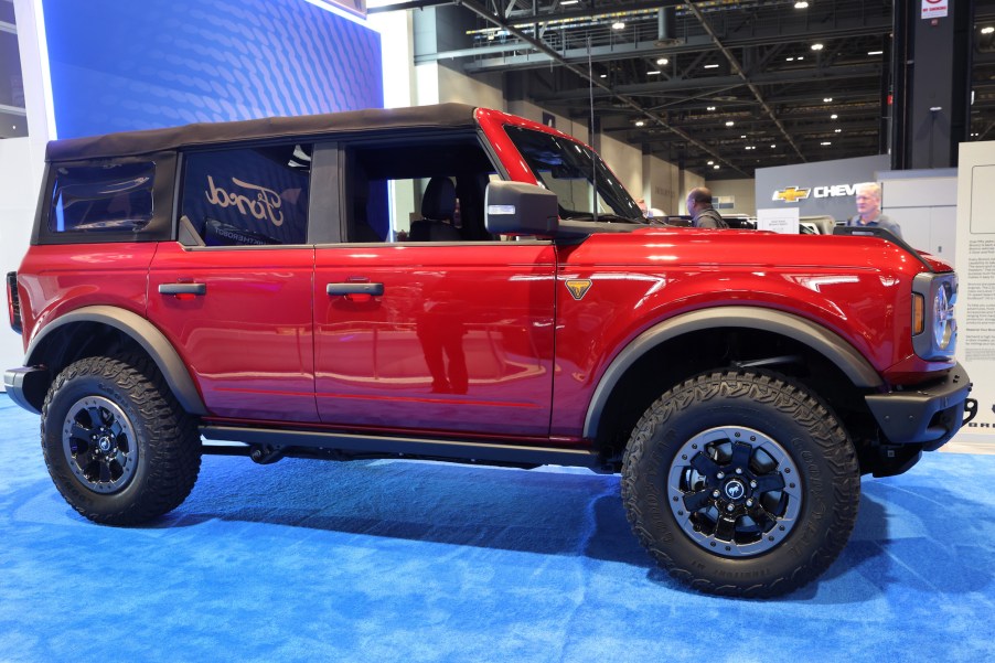 One of the red new Ford Bronco models on a blue floor parked indoors in front of a purple background.