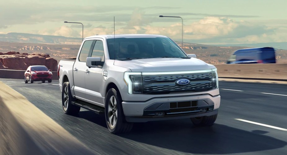 A gray 2022 Ford F-150 Lightning electric pickup truck is driving on the road.