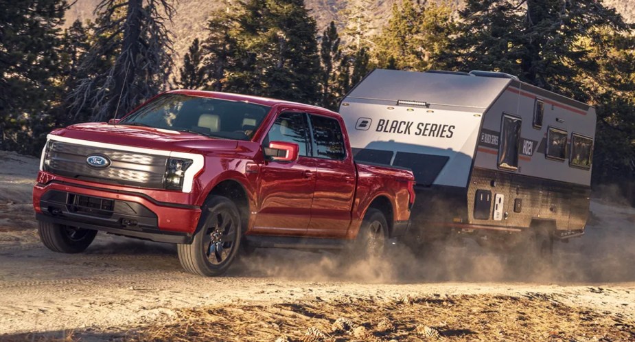 A red 2022 Ford F-150 Lightning electric pickup truck is towing an RV.