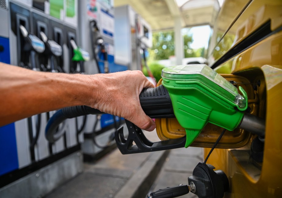 A green nozzle from a gas pump in a yellow car. 