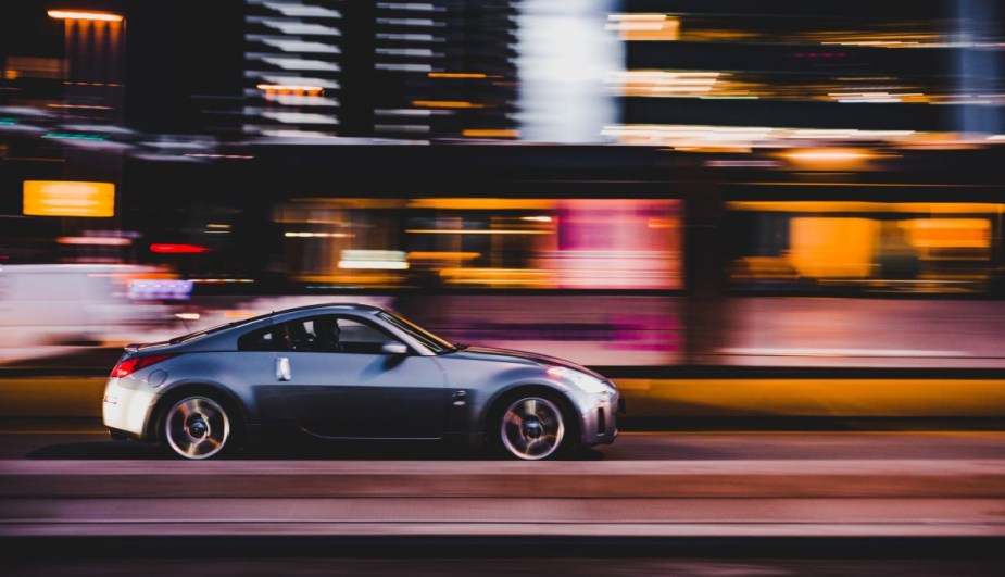 Gray Nissan driving on a street at night, highlighting why cars can drive faster than the speed limit