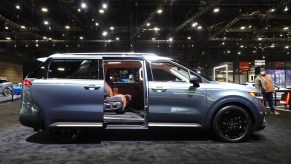 A silver Kia Carnival with the doors open parked indoors.