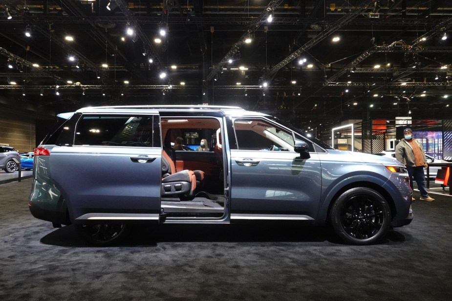 A silver Kia Carnival with the doors open parked indoors. 