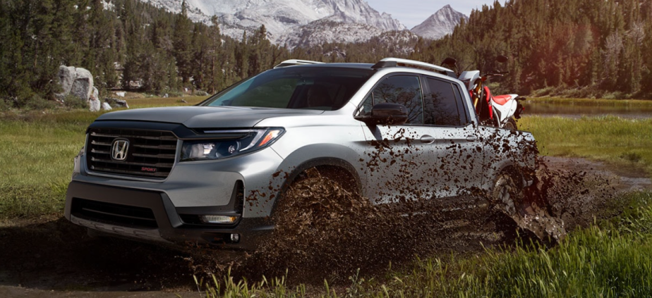 A 2023 Honda Ridgeline off-roads with a dirt bike in its bed.