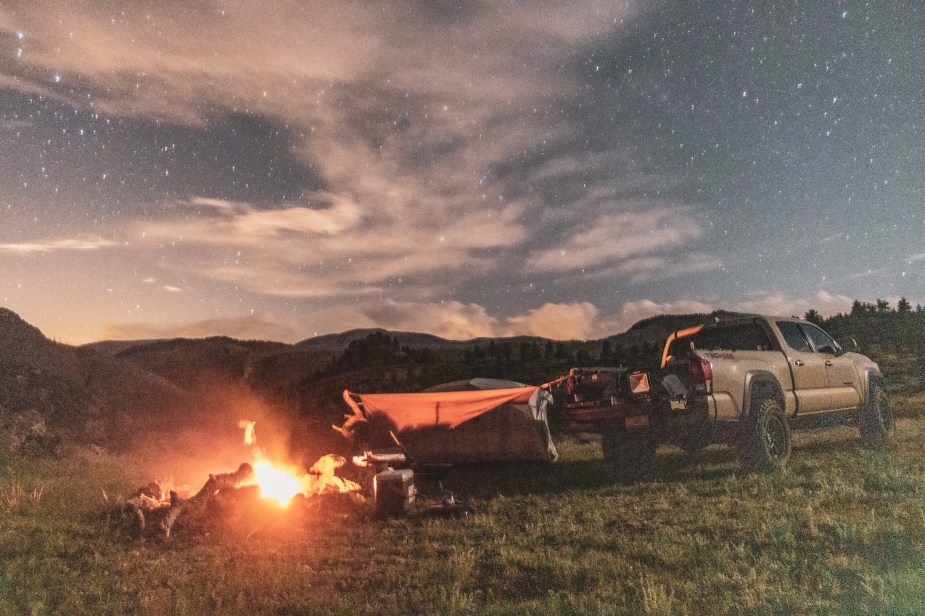 Shot of a Tacoma pickup truck parked in the mountains, a tent set up next to it and a bonfire behind its tailgate.