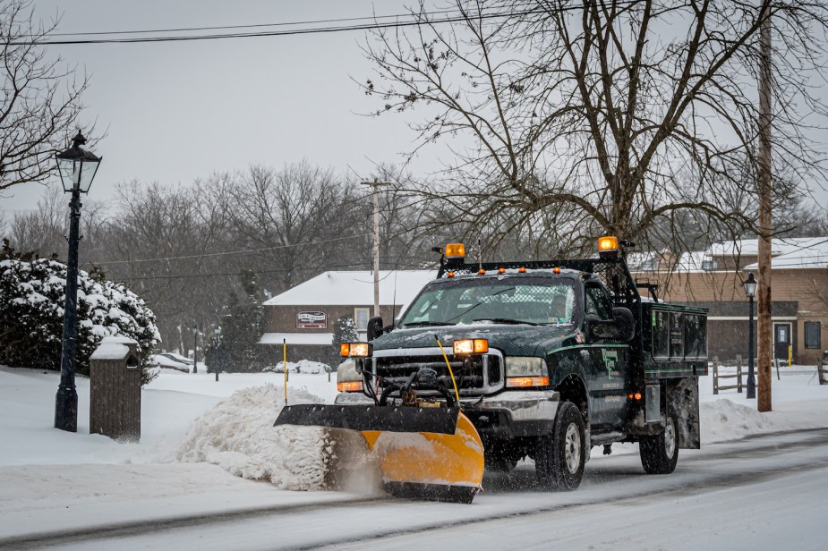 A pickup truck plowing a street with strobing yellow rooftop emergency lighting.