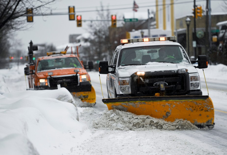 Two plow trucks driiving down the street with yellow rooftop lights.