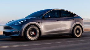 A gray Tesla Model Y electric SUV is driving on the road.