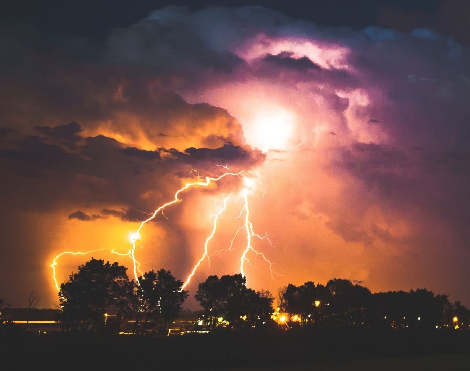 Thunder and lightning over trees, highlighting why loud noises trigger a car alarm