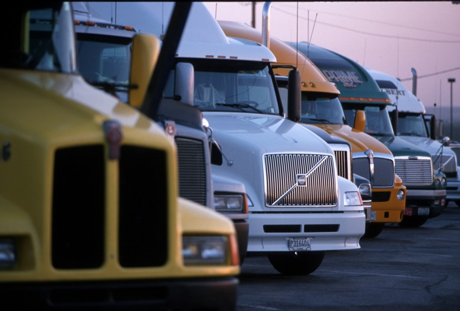 A row of semi truck tractors parked in a lot underneath a twilight sky.