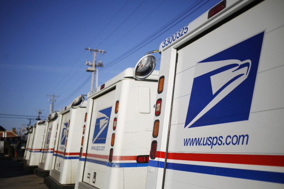 A group of USPS mail trucks sit parked.