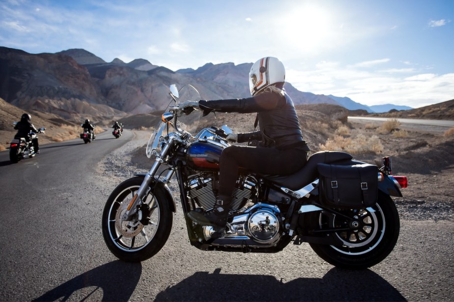 A Harley-Davidson motorcycle rider navigating a hairpin turn in the mountains, other riders visible in the background.