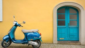 Blue Vespa scooter parked on a cobblestone street with a blue door visible in the background.