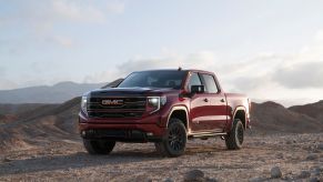 A red 2022 GMC Sierra 1500 AT4X full-size pickup truck model parked on a dirt plain amidst hills and mountains