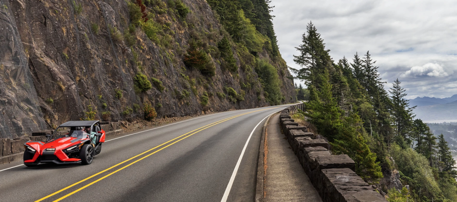 A red 2022 Polaris Slingshot drives down a mountain road.