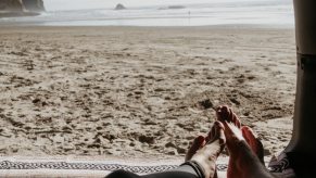 The view from a car parked on the beach, two people's feet visible in the foreground, the ocean in the background.