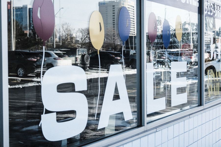 A used car dealership window 'SALE' sign and reflection of models on the lot in Detroit, Michigan