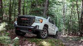 A white 2022 GMC Canyon AT4 midsize truck model (available in diesel) traveling off-road through a forest