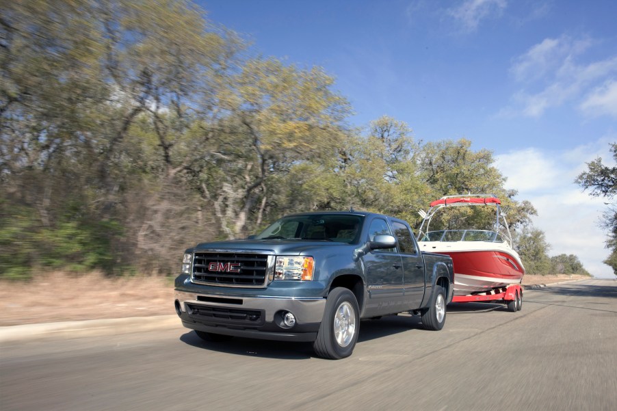 Promo photo of a GMC Sierra full-size hybrid pickup truck towing a boat down a rural road, trees visible in the background.