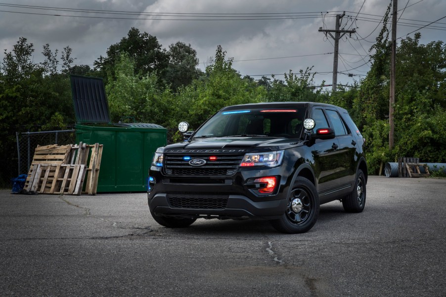 A Ford police Interceptor SUV stopped in a parking lot, a dumpster and trees visible in the background.