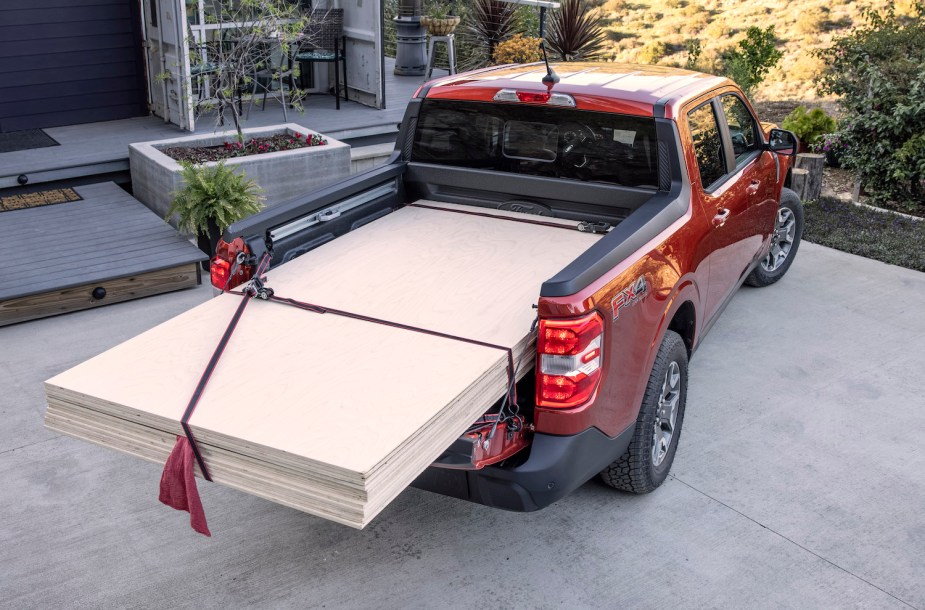 Red Ford Maverick compact truck loaded with a stack of plywood sheets, parked in front of a house.