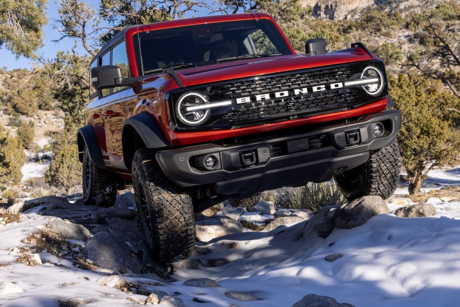 A red 2022 Ford Bronco Wildtrak off-road compact SUV driving on snow-covered rocks