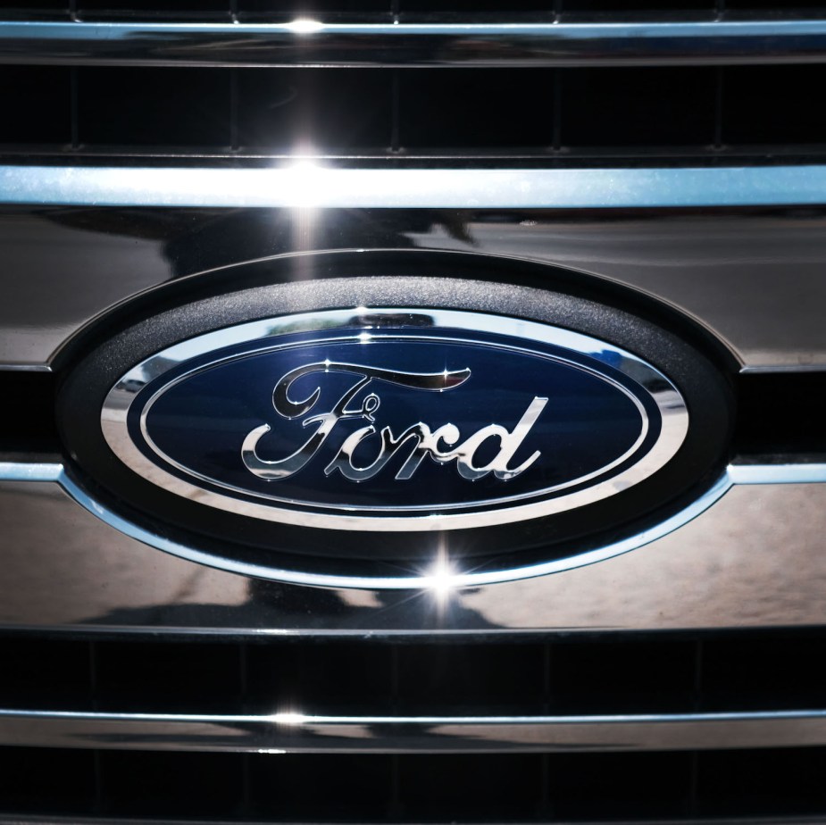 Closeup of Ford's Blue Oval logo in the chrome grille of a hybrid PowerBoost F-150 pickup truck.