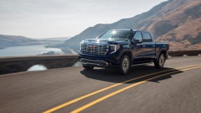 A dark colored 2022 GMC Sierra driving alongside a lake and mountains.