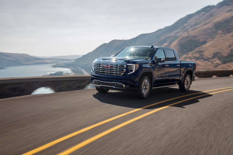 A dark colored 2022 GMC Sierra driving alongside a lake and mountains.