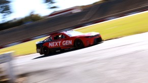 Nascar stock car completing practice laps on a race track, grass visible in the background.