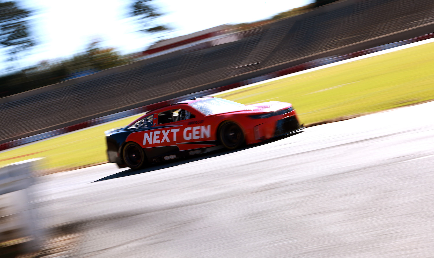 Nascar stock car completing practice laps on a race track, grass visible in the background.