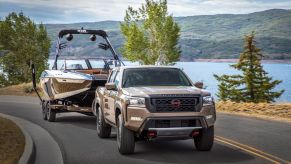 A bronze 2022 Nissan Frontier compact pickup truck towing a speedboat near a lake