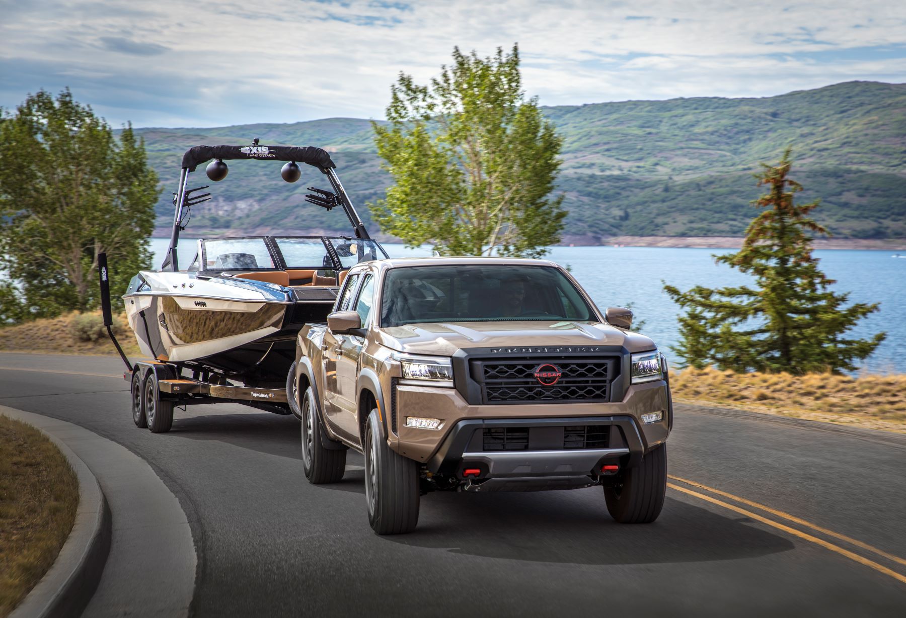 A bronze 2022 Nissan Frontier compact pickup truck towing a speedboat near a lake