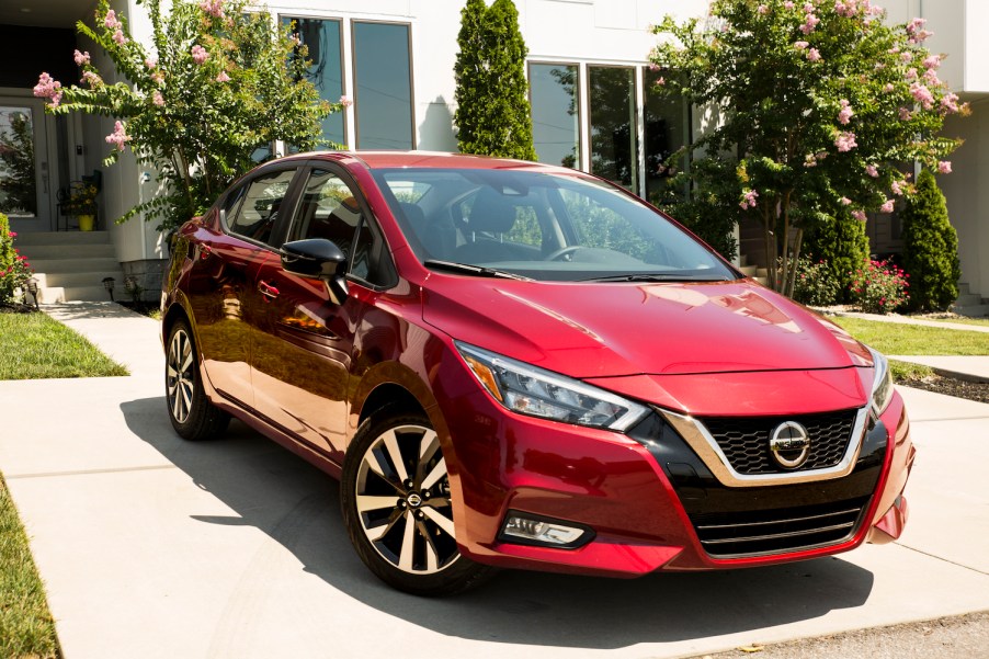 A red 2022 Nissan Versa subcompact car parked in front of a garage