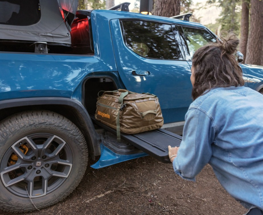 A Rivian driver slides a duffel bag into the electric truck's gear tunnel under its bed.