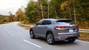 A silver 2022 Volkswagen Atlas Cross Sport driving down the highway in a wooded area.