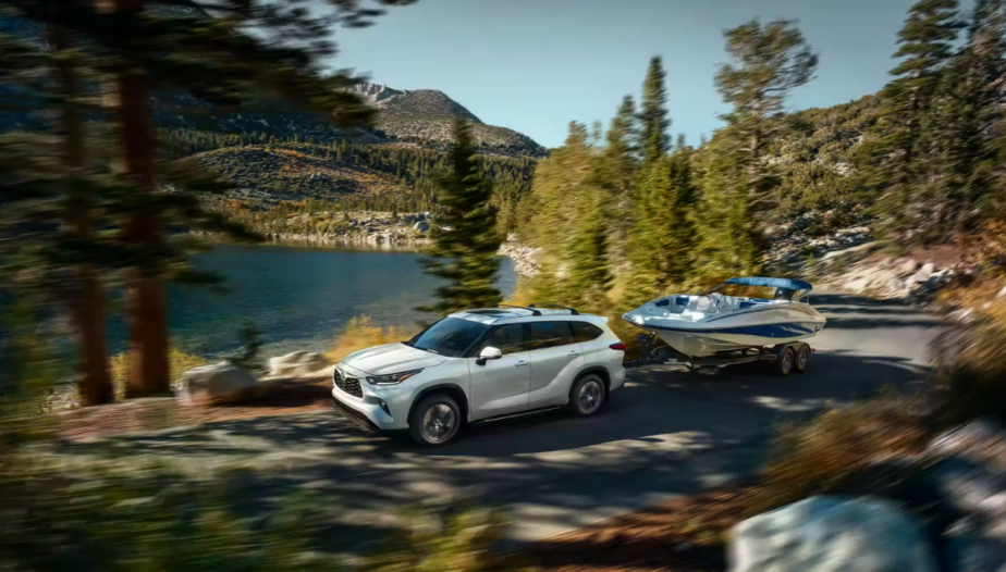 A 2022 Toyota Highlander Hybrid tows a boat behind it as a hybrid SUV.