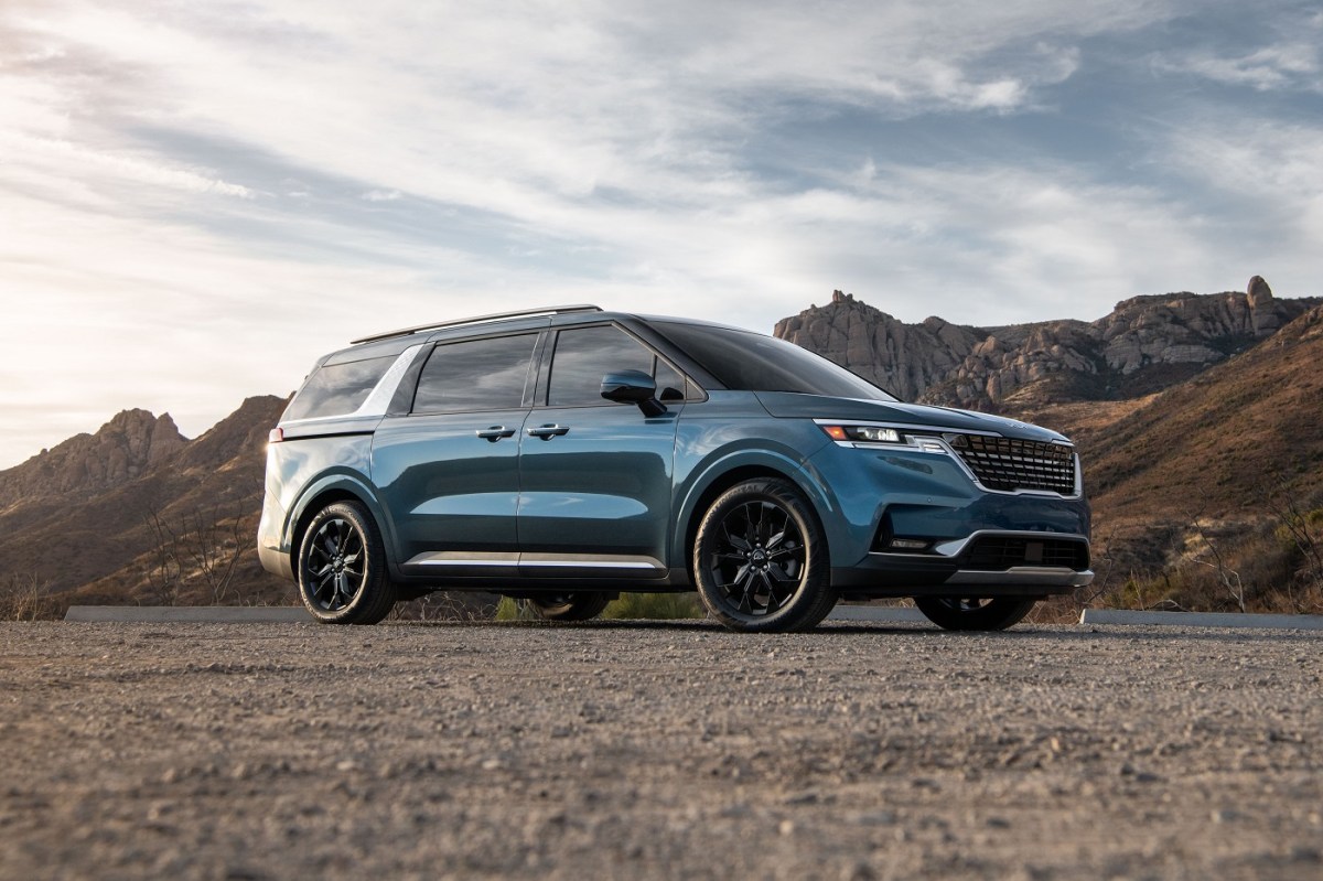 A blue 2023 Kia Carnival parked on a dirt lot.   