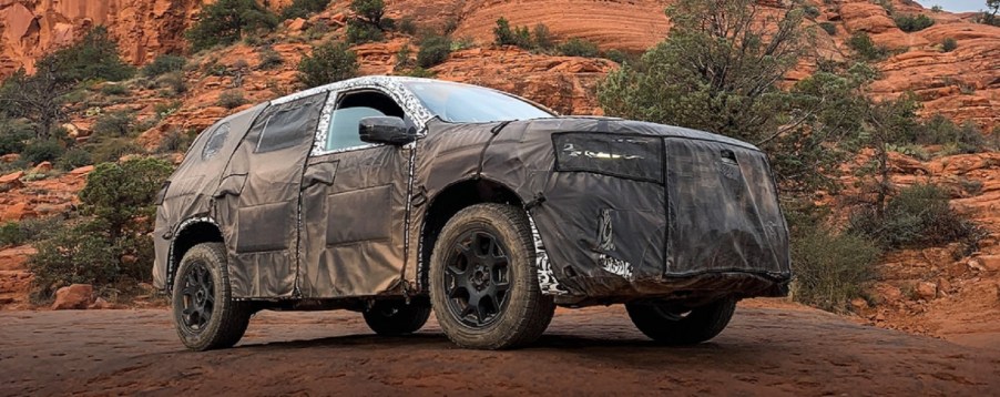 A camoflauge-wrapped 2023 Honda Pilot against trees.