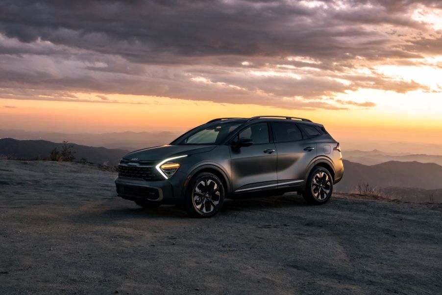 A 2023 Kia Sportage PHEV compact SUV parked on a sandy cliff at sunset with its headlights on