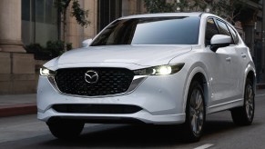 A white 2023 Mazda CX-5 small SUV is driving on the road.