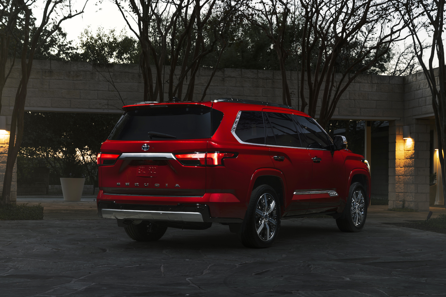 Red Toyota Sequoia full-size large hybrid SUV parked in a driveway at dusk.