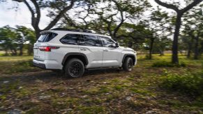 White Toyota Sequoia TRD Pro hybrid 3rd row SUV, driving through the woods, blurry trees visible in the background.