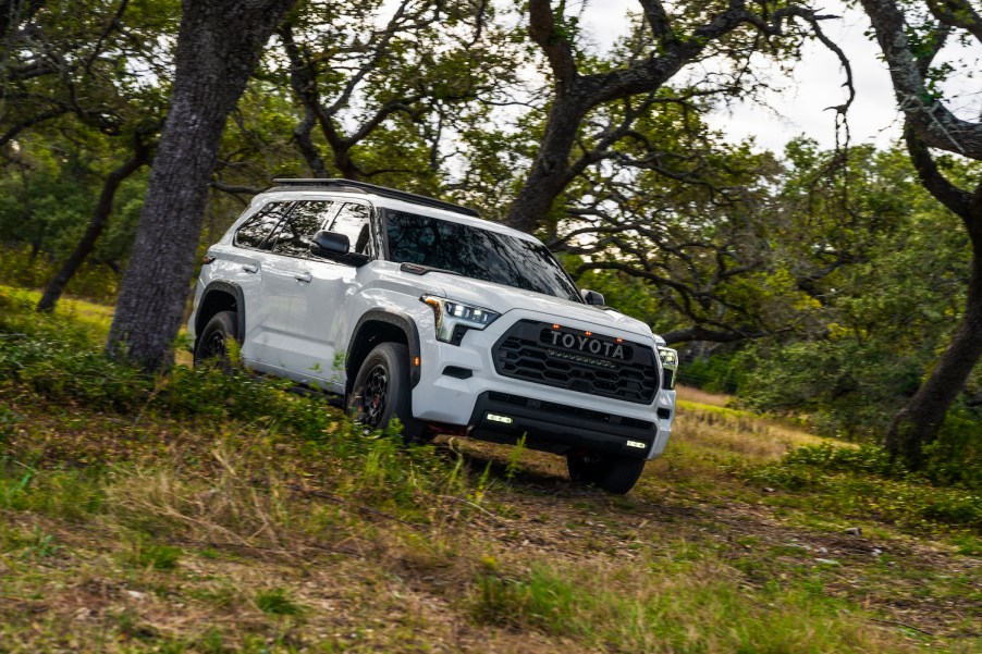 White Toyota Sequoia TRD Pro SUV off-roading, grass visible in the foreground and trees visible behind it.